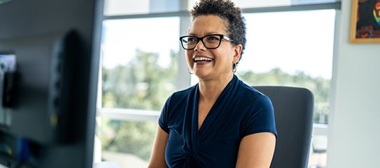 A Canadian healthcare professional sitting at a desk smiling during a virtual consultation.