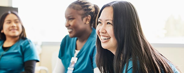 Three female nurses smiling in a hospital conference room.