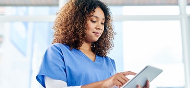 Canadian healthcare professional in blue scrubs usings a tablet to find resourceful tools for her practice